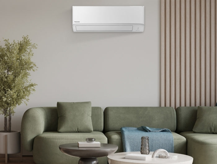 Modern living room with a green couch below a white wall-mounted air conditioner unit