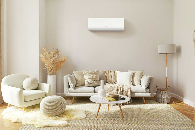 A bright living room with a light gray couch and accent chair situated below a TCL wall-mounted air conditioner unit