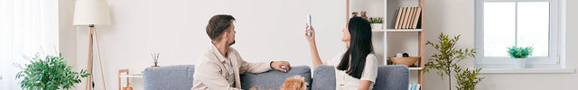 A couple sitting on a couch with their dog, turning on the air conditioner unit