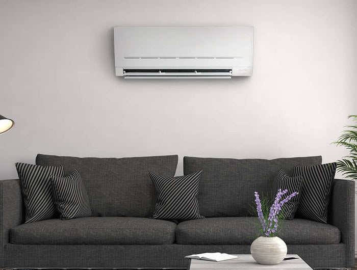 A dark gray couch against a white wall with a Mitsubishi white air conditioner